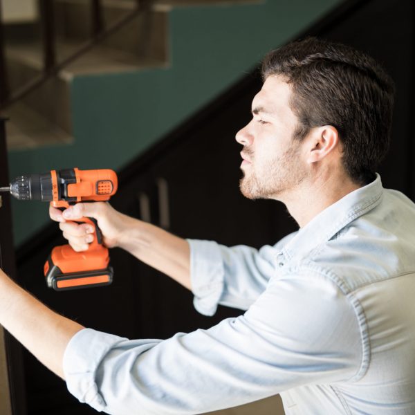 Profile view of an attractive handyman using a power drill to fix a door knob in a house